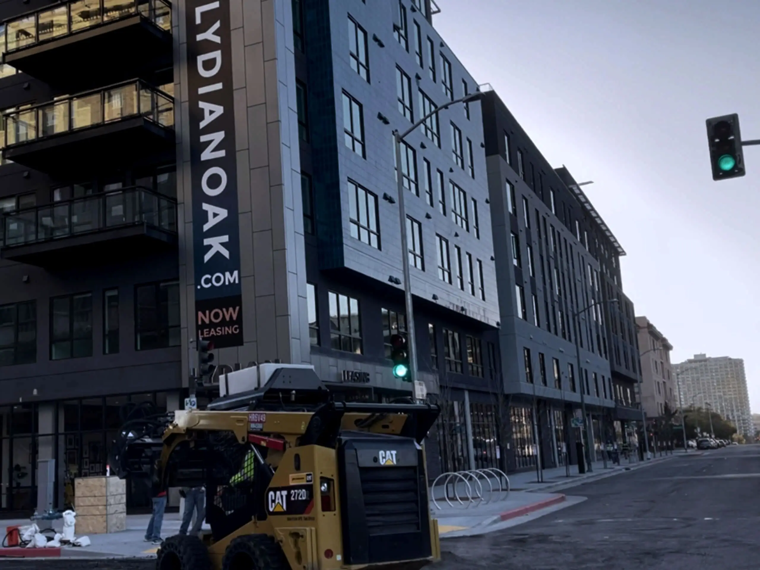A skid steer working at the curb line in front of the Lydian Oakland building.