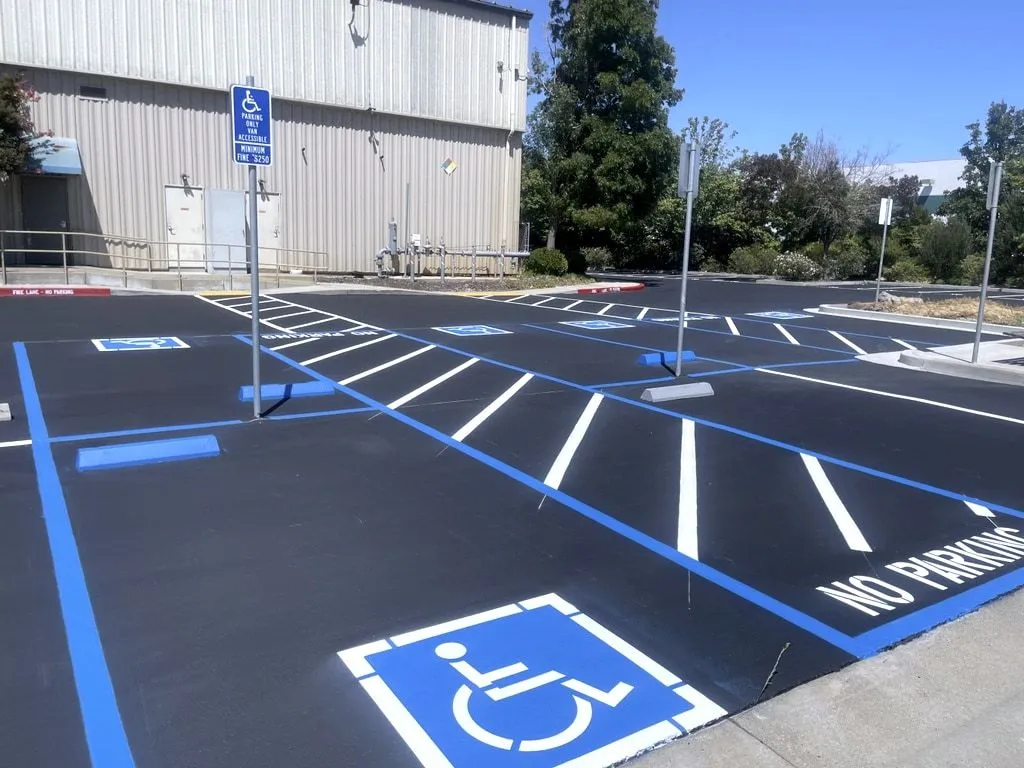 Newly striped accessible parking stalls in blue, with the wheelchair symbol, a no-parking access aisle and posted accessible parking signs.