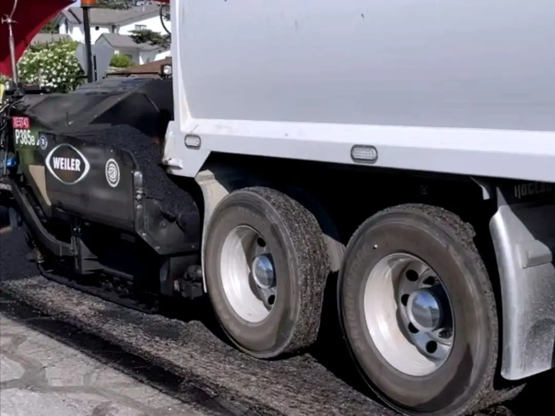 A paving truck working the full width of a narrow hillside residential street.