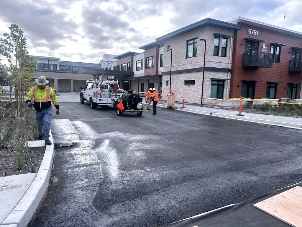 Crew working an entrance drive over fresh black asphalt, in front of the new building numbered 5751.