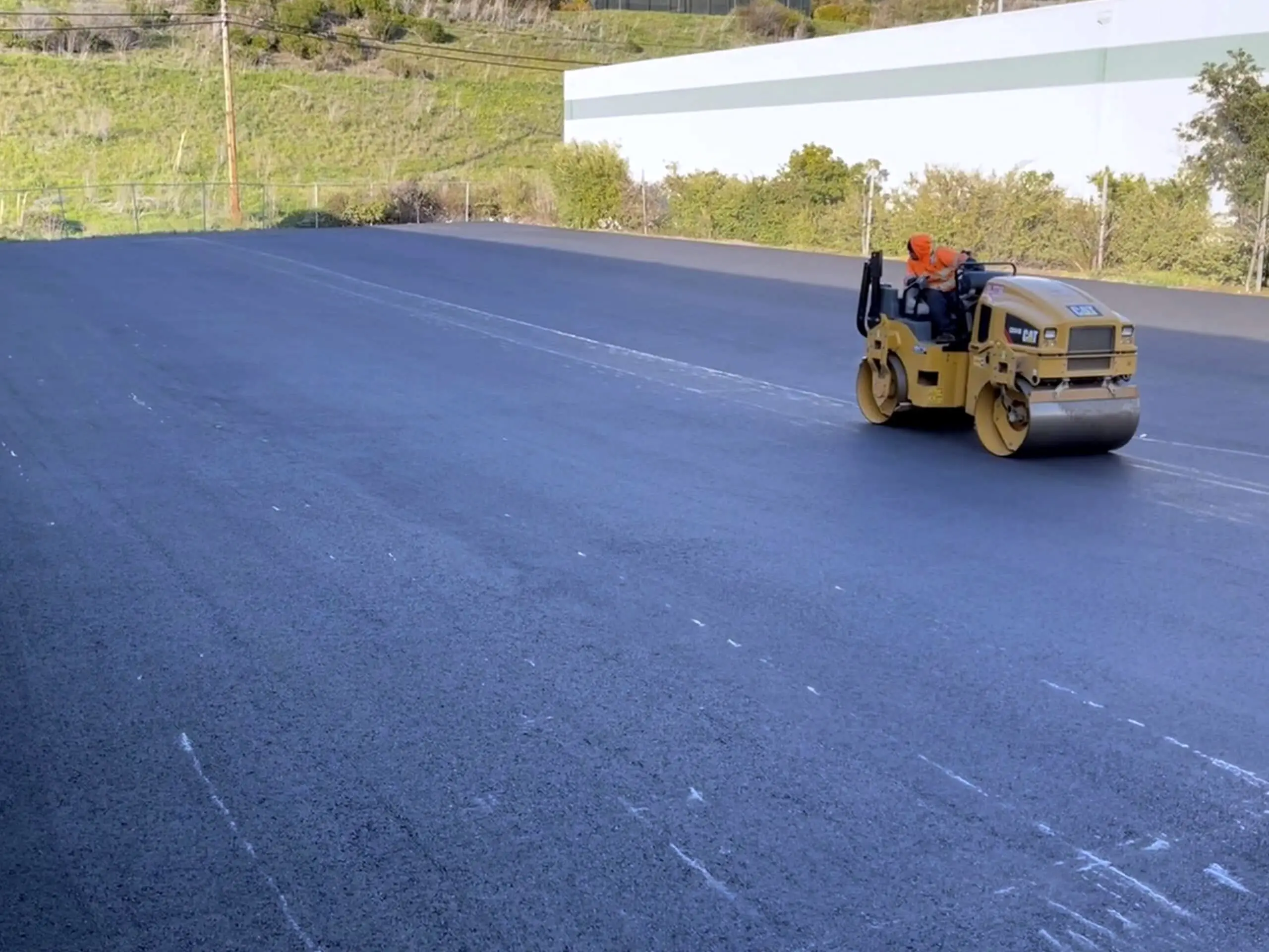 A roller compacting the new asphalt mat alongside the warehouse at Bay Medical Co.