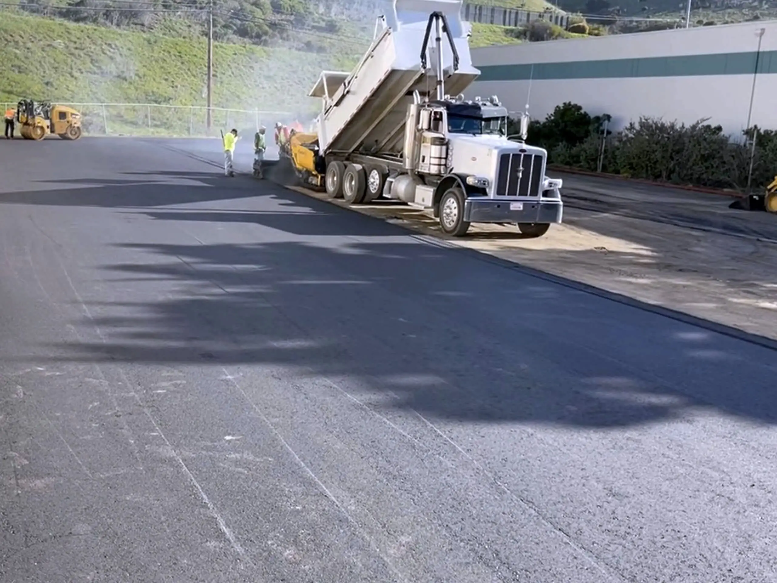 A dump truck feeding the paver as new asphalt is placed across the Bay Medical yard.