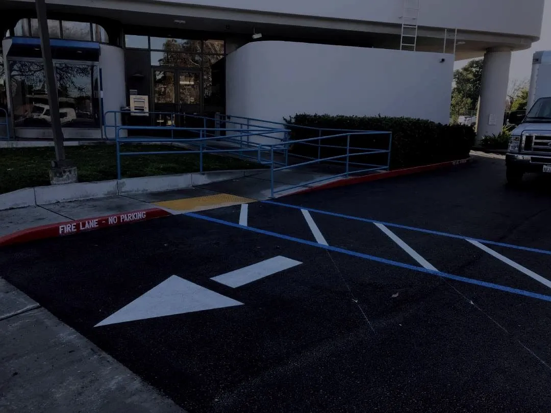 A freshly paved and restriped commercial lot with a new ADA ramp, detectable warning pad and red fire lane curb.