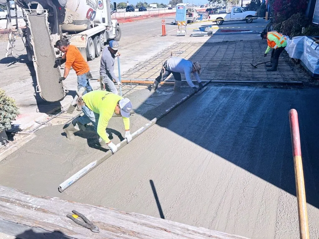 A Forticon crew screeding a new concrete ADA parking stall as the mixer truck pours alongside, with rebar mesh set in the next section.
