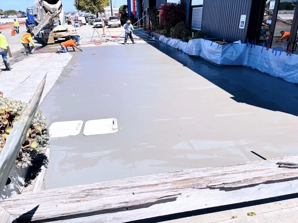A freshly placed concrete slab being finished beside a mixer truck at a commercial site.
