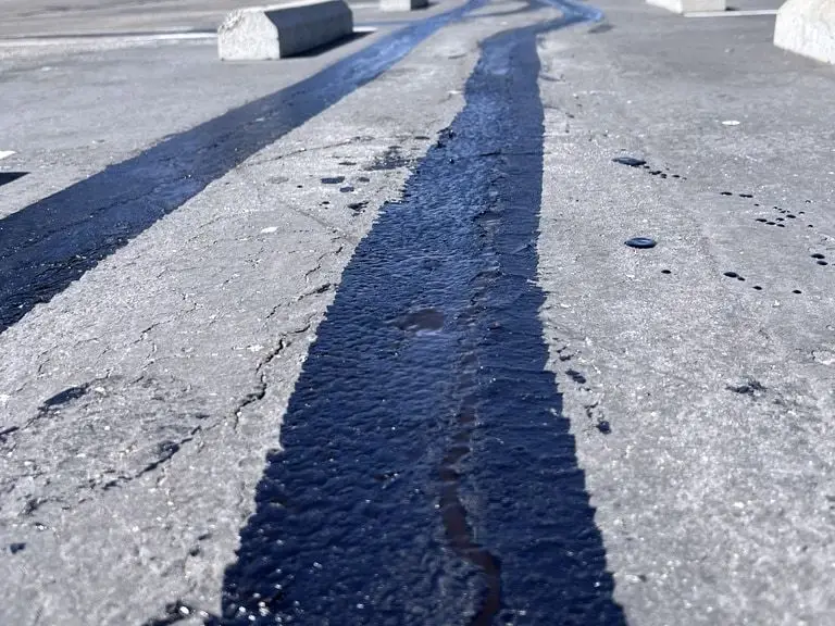 Fresh black sealant bands filling cracks in the gray asphalt of a parking lot.