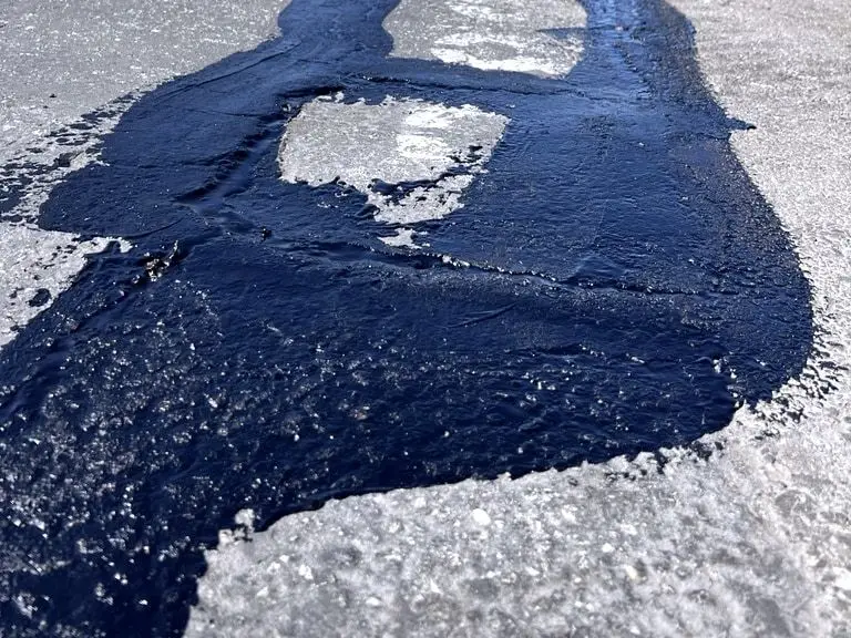 A wide pour of fresh black sealant over cracked, worn pavement.