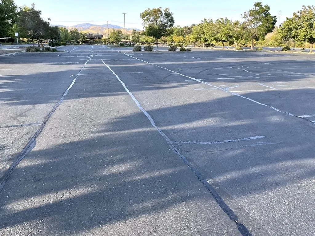 A large commercial parking lot with its cracks filled, the dark sealant lines running across the faded asphalt.
