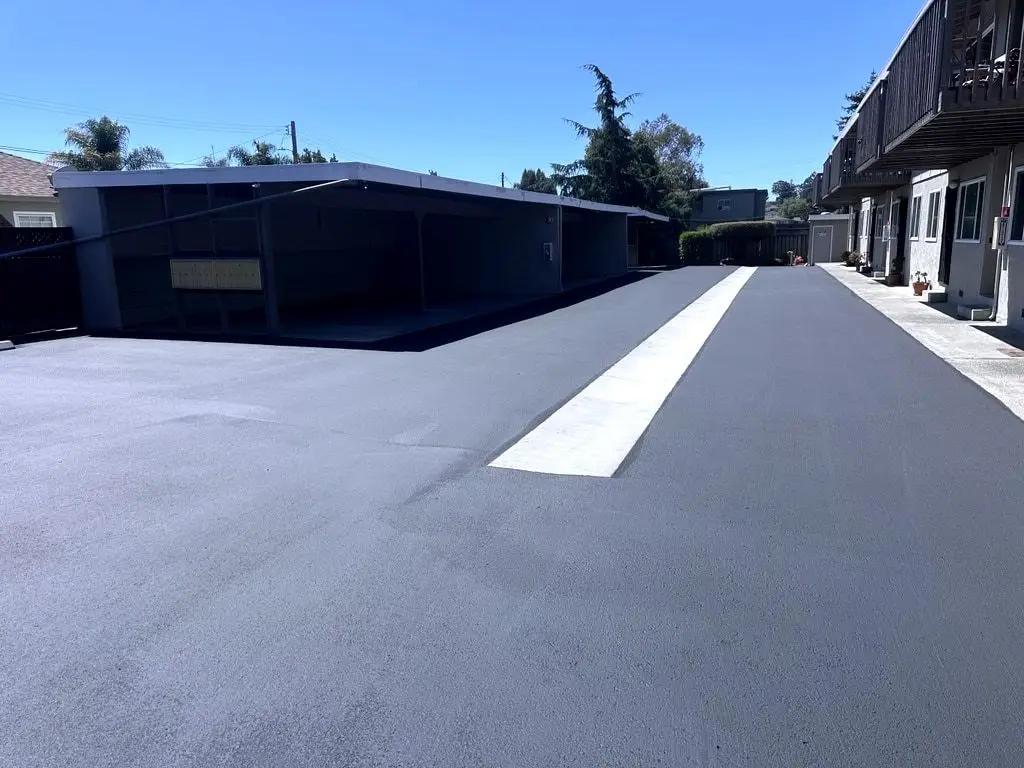 The finished alley: fresh black asphalt with the white concrete gutter running through it, carports on the left.