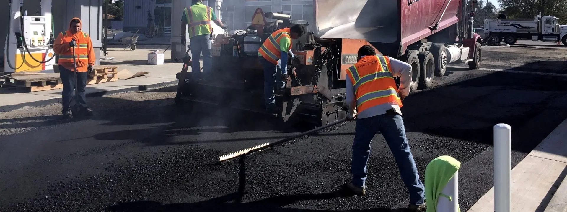 A Forticon crew working the mat behind the paver, with steam rising off freshly placed hot-mix asphalt.