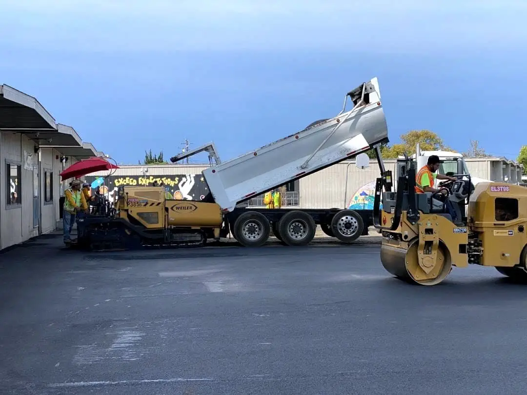 Hot-mix asphalt discharging from the truck bed into the paver hopper on the Longwood school site.