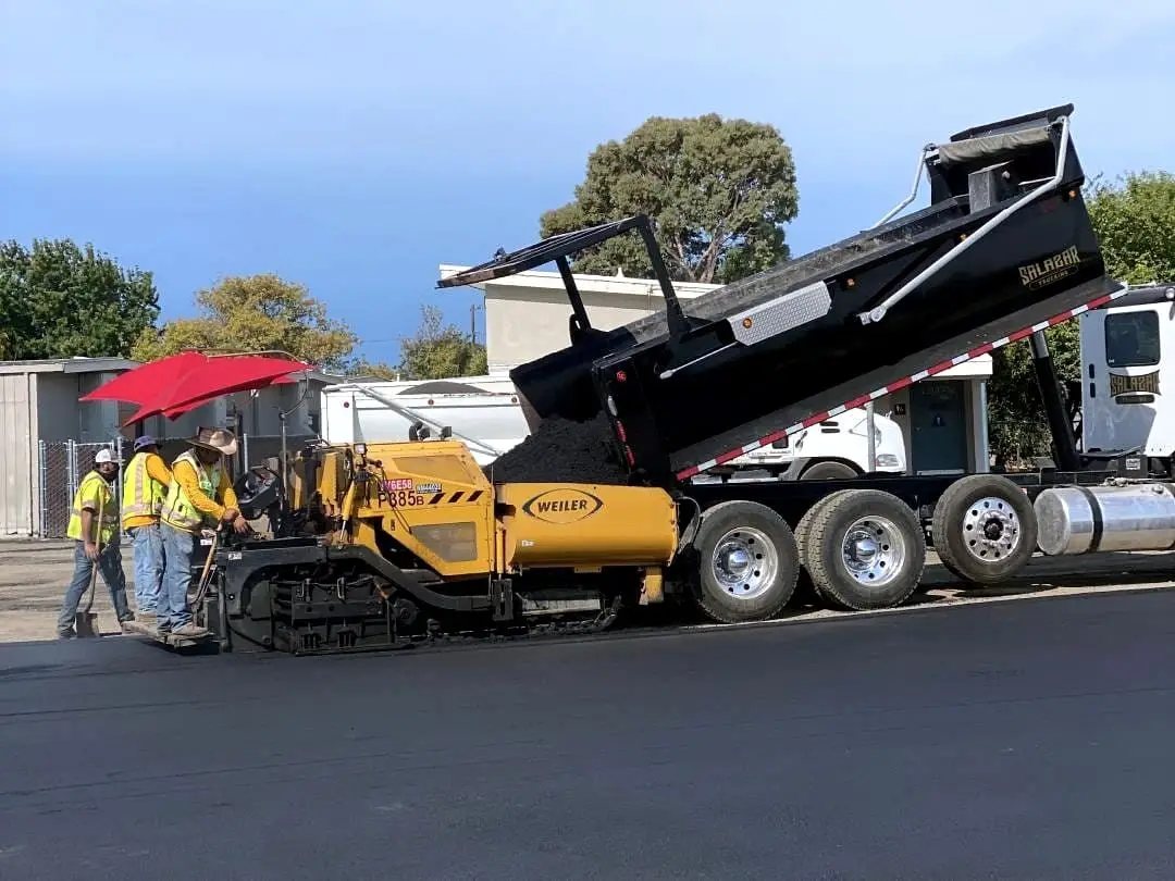 The paving train of truck, paver and crew placing asphalt across the Longwood Elementary playground.