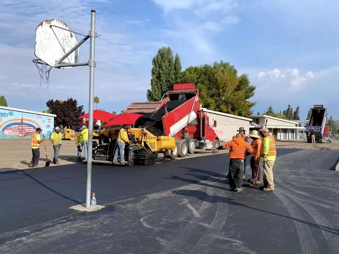 Forticon crew alongside the paver on the newly surfaced playground, with a basketball hoop overhead.