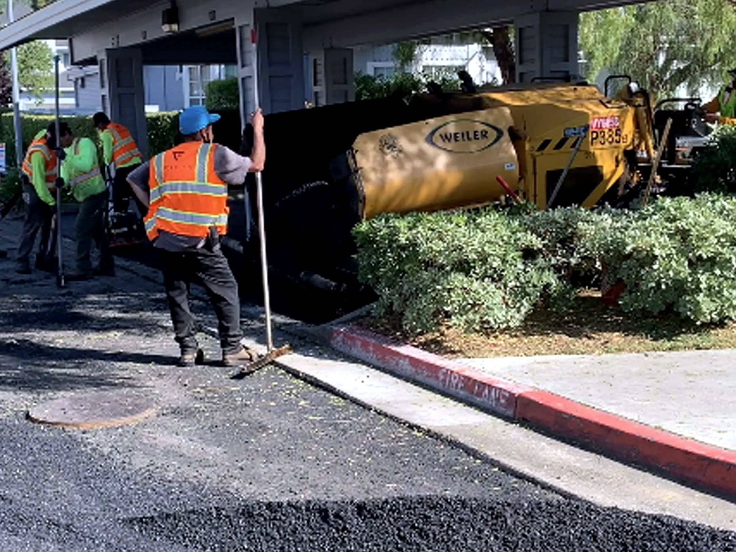 A crew member hand-working the asphalt edge against a driveway and red curb at Marin Lagoon.