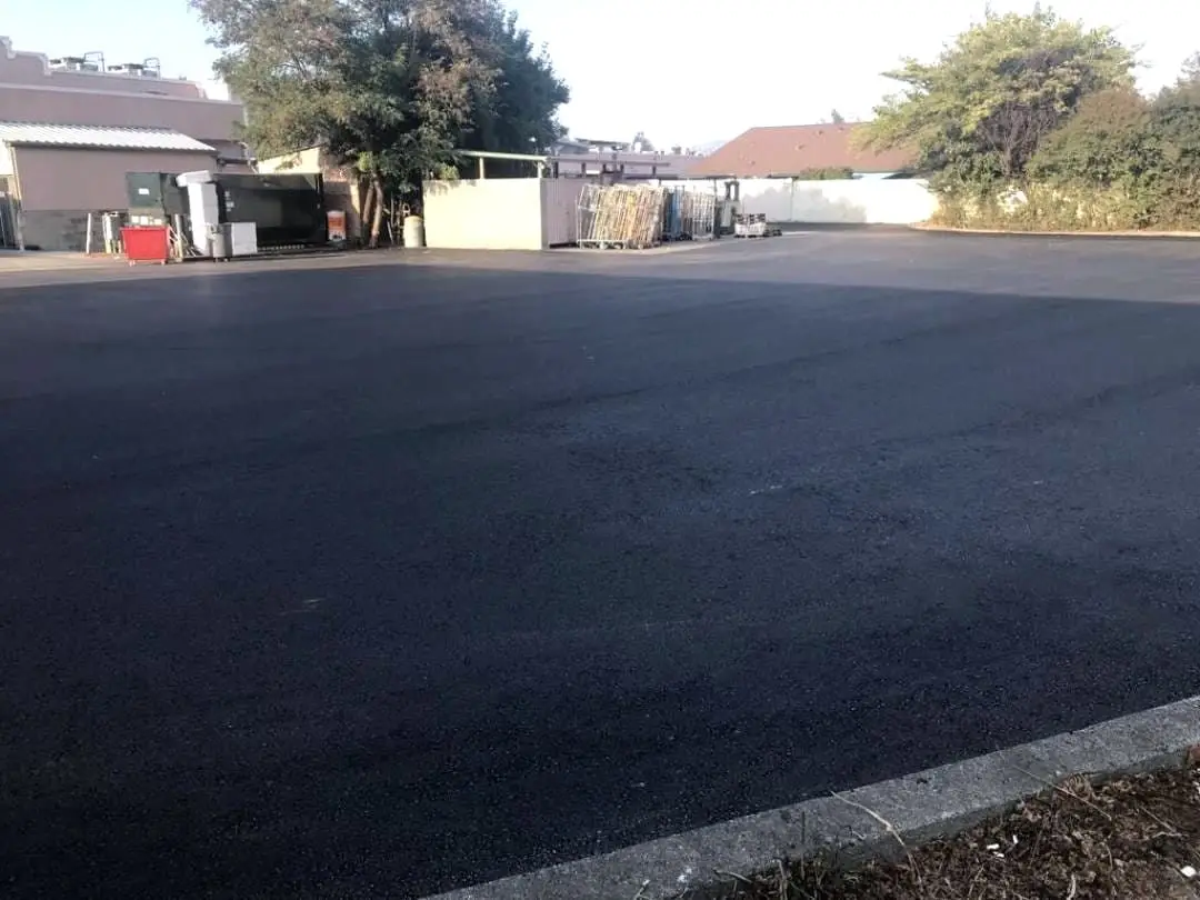 A roller compacting the new asphalt across the Rancho Cotati parking field, with the retail units behind.