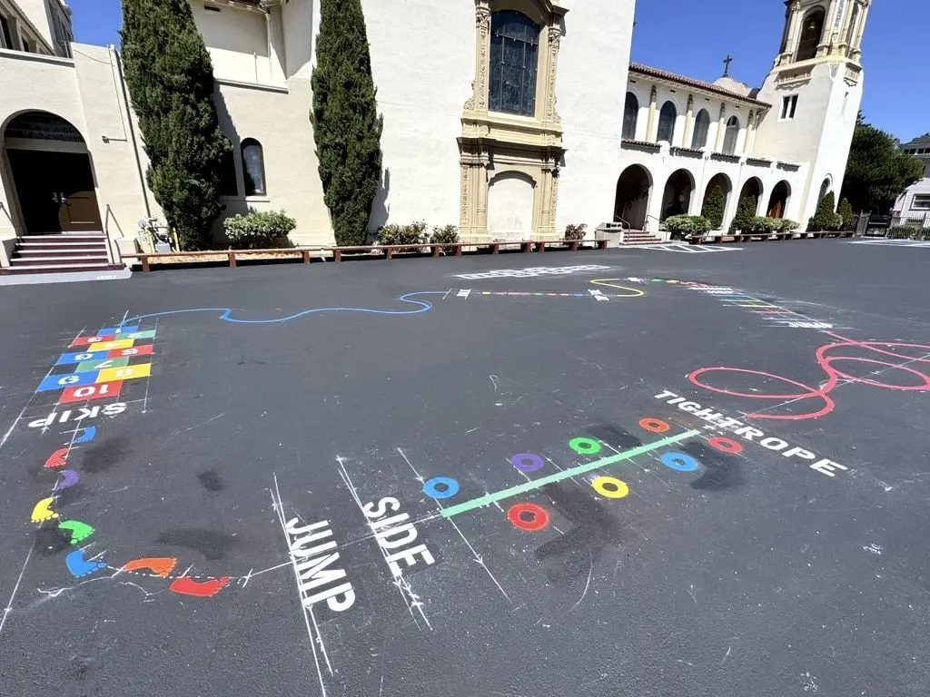 A freshly sealed school yard with colorful painted hopscotch, jump and tightrope games in front of the school building.