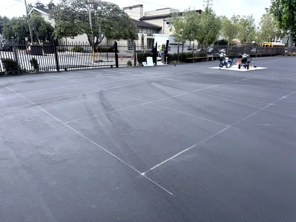 The sealed yard with a chalk layout grid marked out and two striping machines waiting on a tarp.