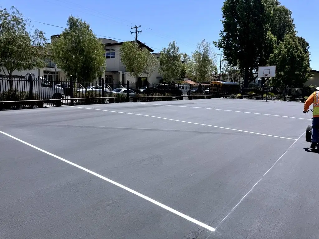 White court lines on the fresh dark surface, with a worker and equipment at the edge of the frame.