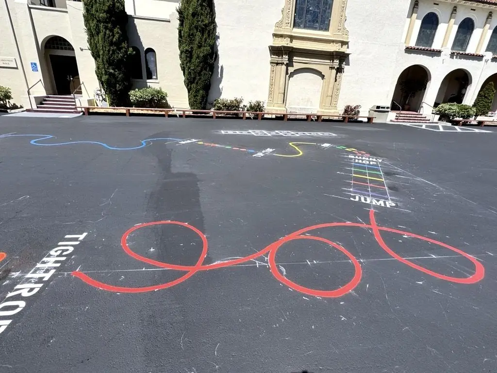 Painted playground games, including rainbow lines, a red figure-eight and lettered jump and tightrope paths.
