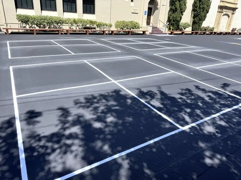 Newly painted four-square courts in white on the dark surface, with the school building behind.