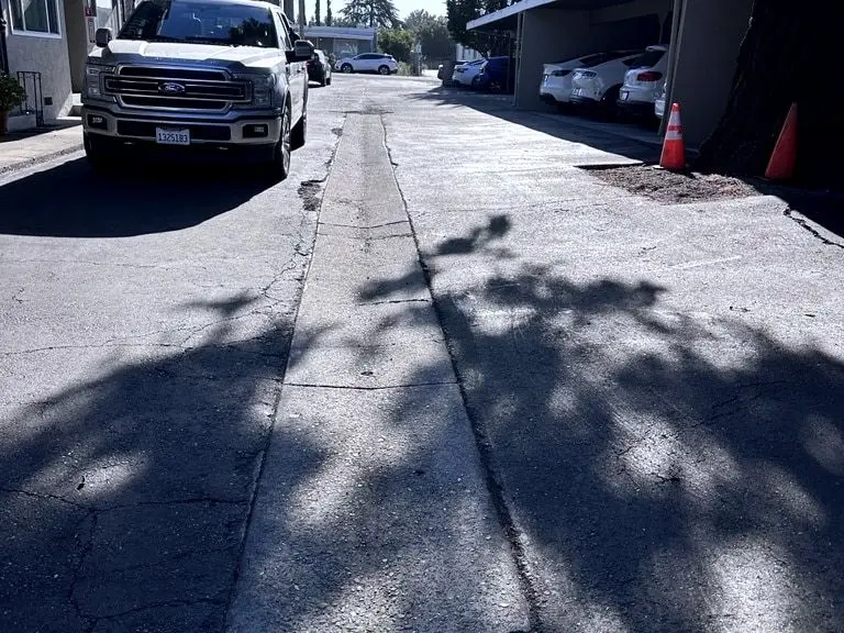 The alley before work: worn, cracked pavement with a strip down its center, with carports on one side and apartments on the other.